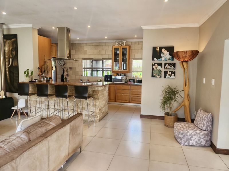 Open-plan living and kitchen area featuring a stone-clad breakfast bar, wooden cabinetry, and neutral tiled flooring with recessed lighting.