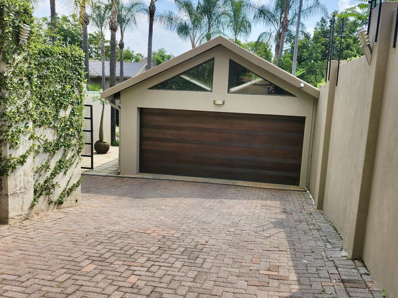 A well-maintained detached garage featuring a timber sectional door, paved driveway, and secure perimeter wall with electric fencing.