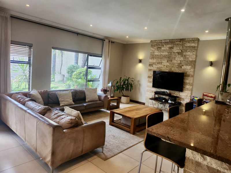 Spacious open-plan living area featuring a stone-clad feature wall, tiled flooring, recessed lighting, and a granite breakfast bar overlooking the lounge.