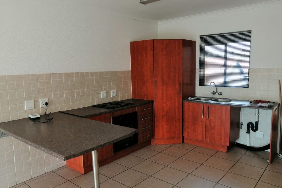 A functional kitchen featuring wood-finish cabinetry, laminate countertops, built-in oven and hob, tiled backsplash, and tiled flooring. Requires minor repairs to cabinetry.