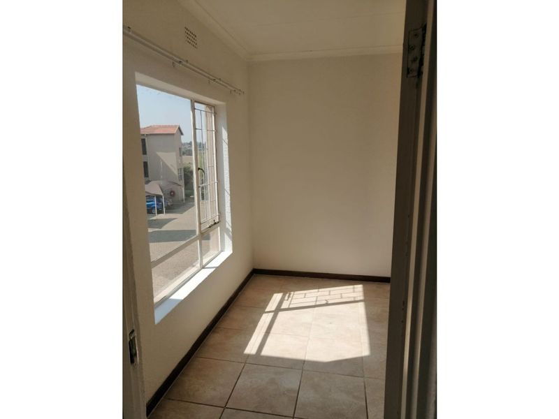 A bright, empty bedroom featuring tiled flooring, a large window with a curtain rail, and neutral wall finishes.