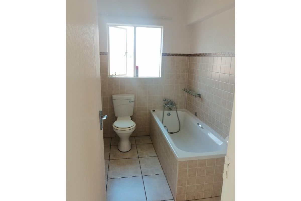 A functional bathroom featuring a bathtub with a handheld shower mixer, a standard toilet, and neutral wall and floor tiling.