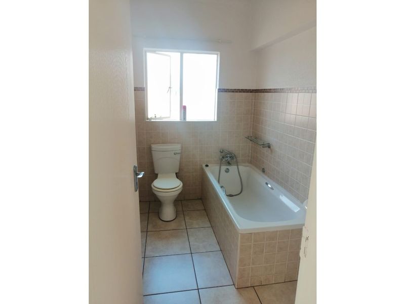 A functional bathroom featuring a bathtub with a handheld shower mixer, a standard toilet, and neutral wall and floor tiling.