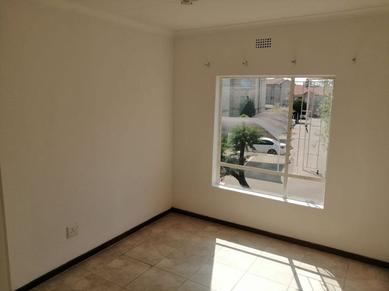 A bright, empty bedroom featuring tiled flooring, a large window with security bars, and neutral wall finishes.