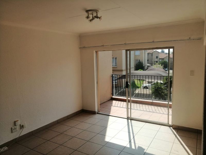 An empty living room featuring tiled flooring and a large sliding glass door that opens onto a private balcony.