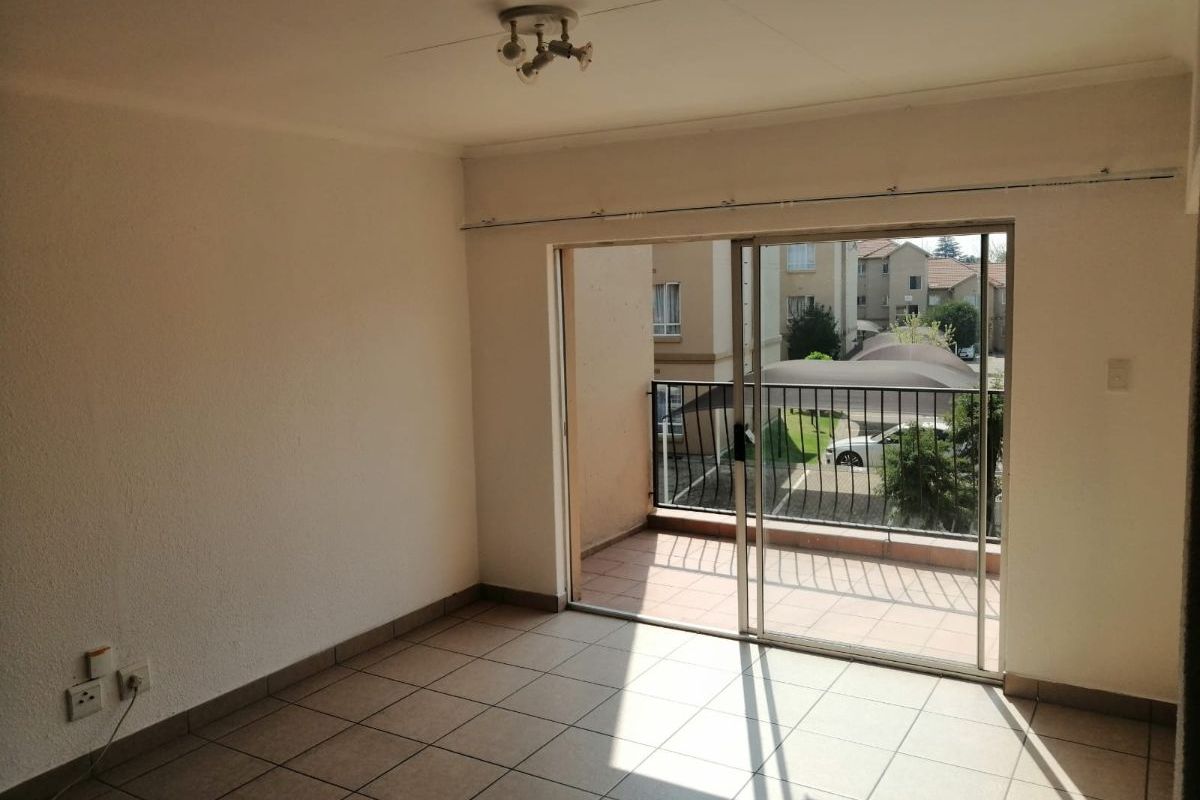 An empty living room featuring tiled flooring and a large sliding glass door that opens onto a private balcony.