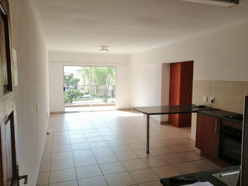 An open-plan living and kitchen area featuring tiled floors, built-in cabinetry, and a sliding door leading to a balcony.