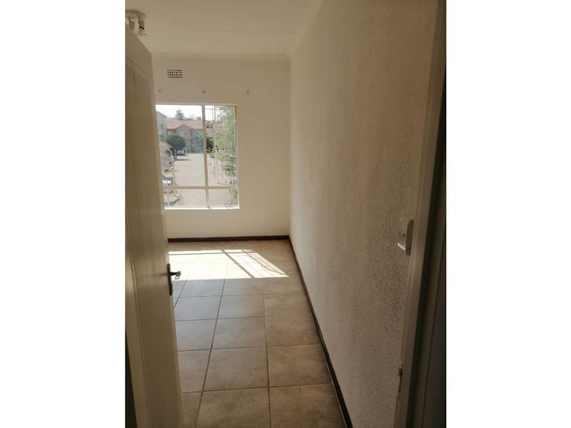 A bright, empty bedroom featuring tiled flooring and a large window with a view of the complex.