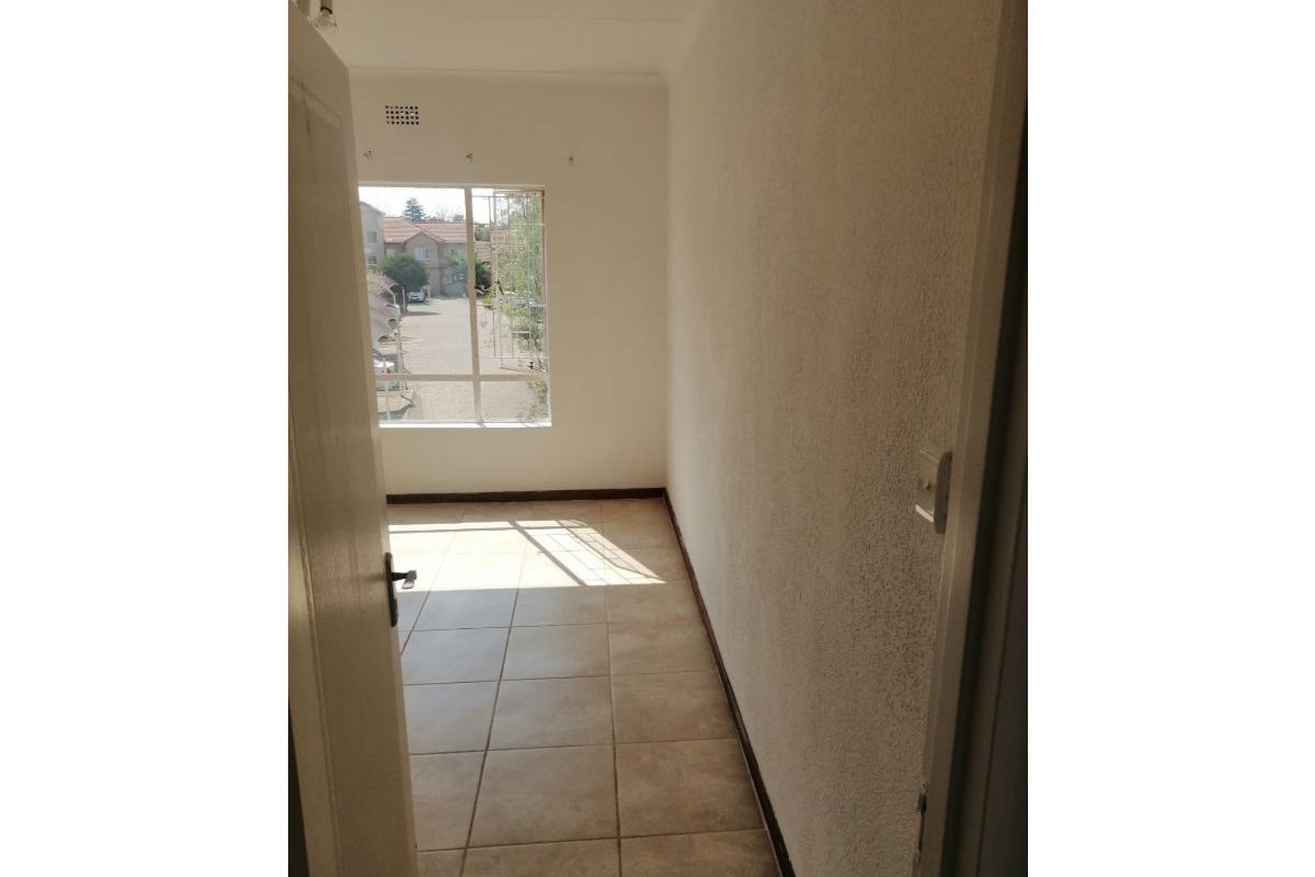 A bright, empty bedroom featuring tiled flooring and a large window with a view of the complex.