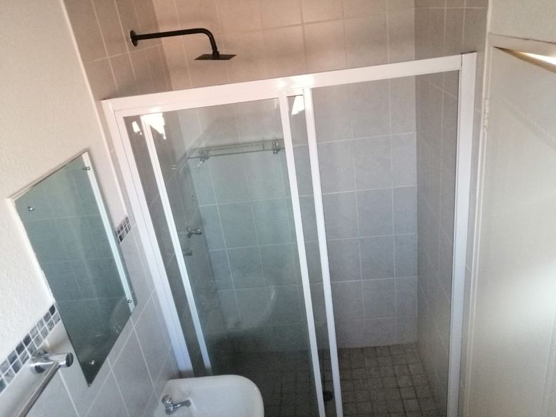 A functional bathroom featuring a glass-enclosed shower, tiled walls and flooring, a pedestal basin, and a wall-mounted mirror.