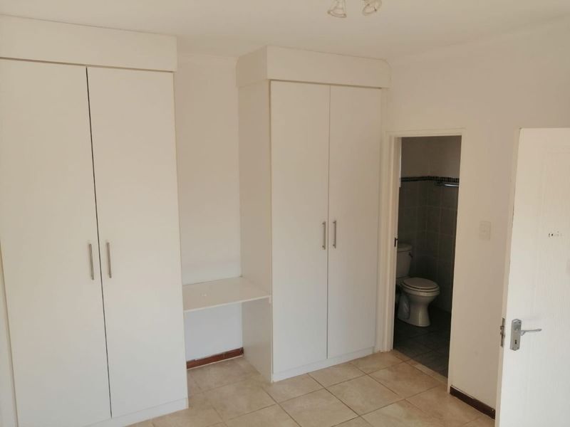 A clean, empty bedroom featuring built-in cupboards with a vanity section and direct access to an en-suite bathroom with tiled flooring.