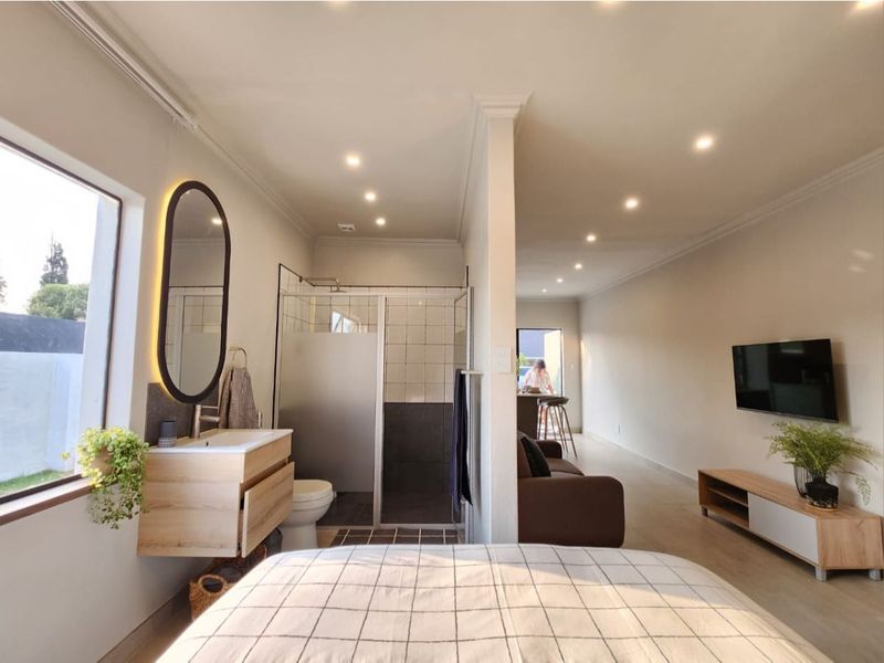 A modern open-plan studio apartment featuring a bedroom area, a contemporary bathroom with a glass-enclosed shower, and a living space with recessed lighting.