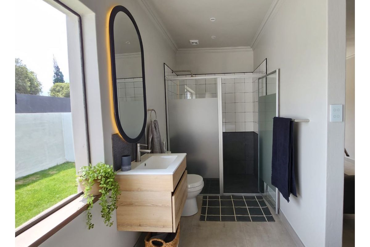Modern bathroom featuring a floating wood-finish vanity, backlit oval mirror, and a walk-in shower with glass enclosure and tiled surround.