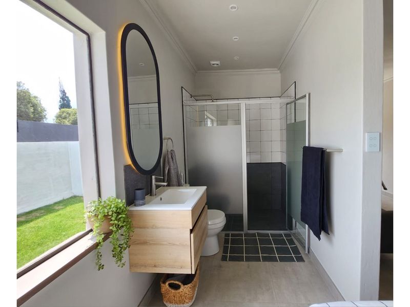 Modern bathroom featuring a floating wood-finish vanity, backlit oval mirror, and a walk-in shower with glass enclosure and tiled surround.