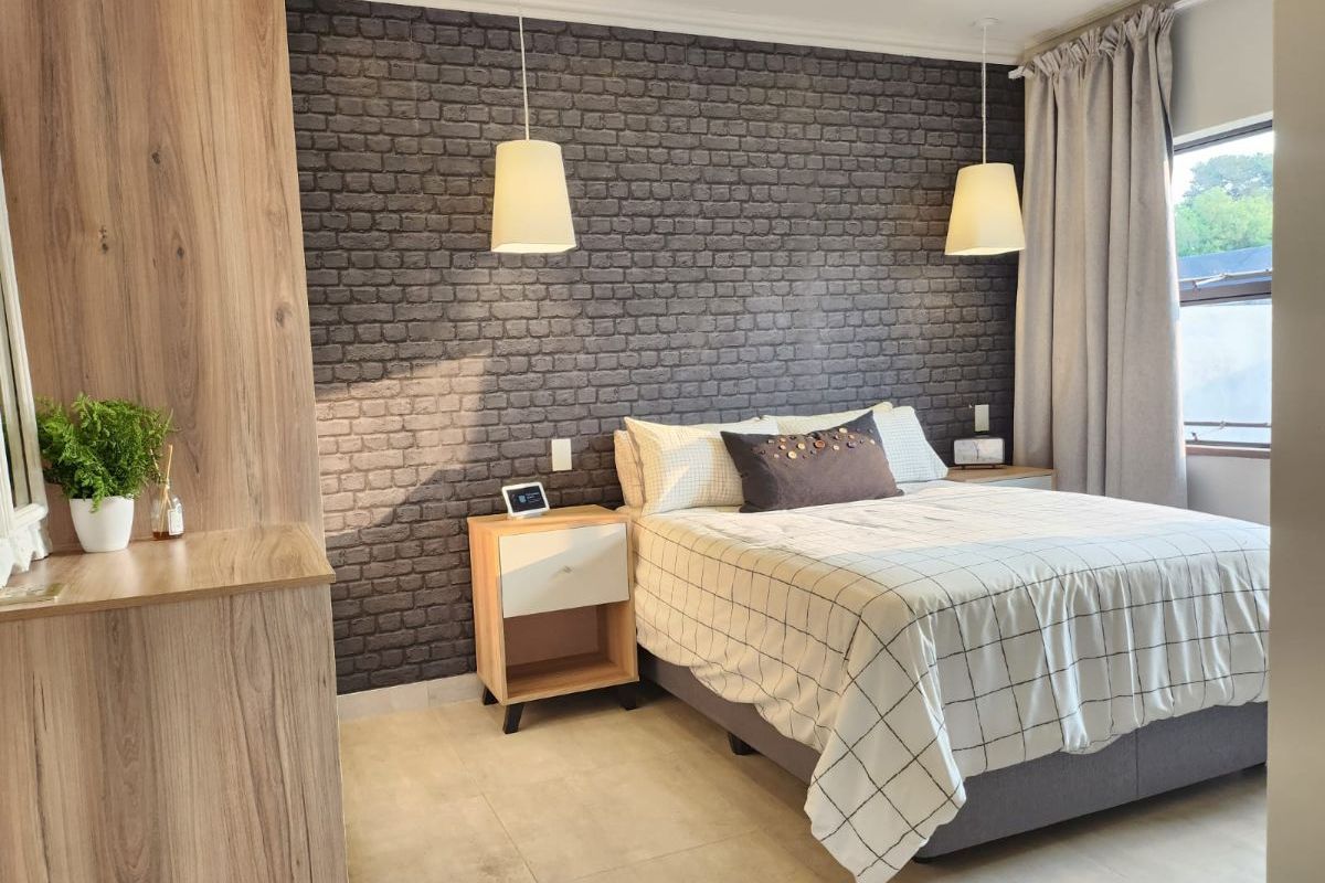 A well-maintained bedroom featuring a textured brick-style accent wall, modern tile flooring, and built-in cabinetry with integrated lighting.