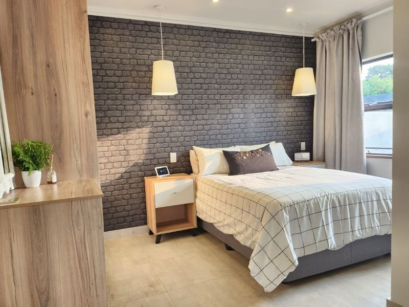 A well-maintained bedroom featuring a textured brick-style accent wall, modern tile flooring, and built-in cabinetry with integrated lighting.