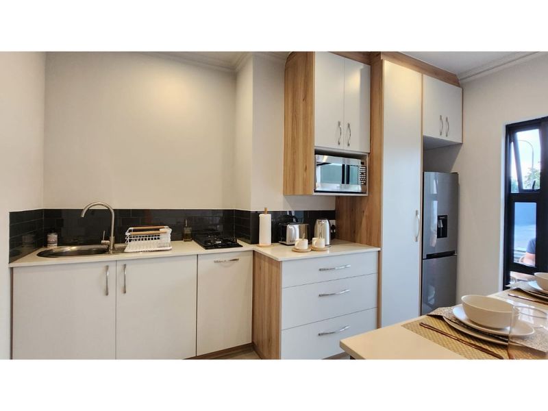 Modern kitchen featuring sleek white cabinetry with wood-grain accents, integrated microwave, gas hob, and a dark tiled backsplash.