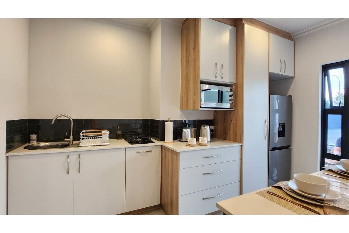 Modern kitchen featuring sleek white cabinetry with wood-grain accents, integrated microwave, gas hob, and a dark tiled backsplash.