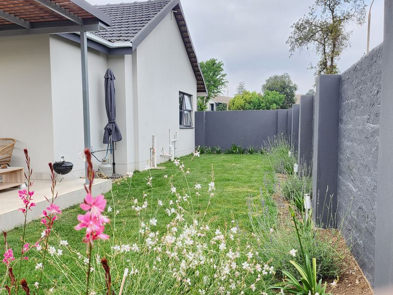 A well-maintained rear garden featuring a paved patio area, a manicured lawn, and a modern perimeter wall.