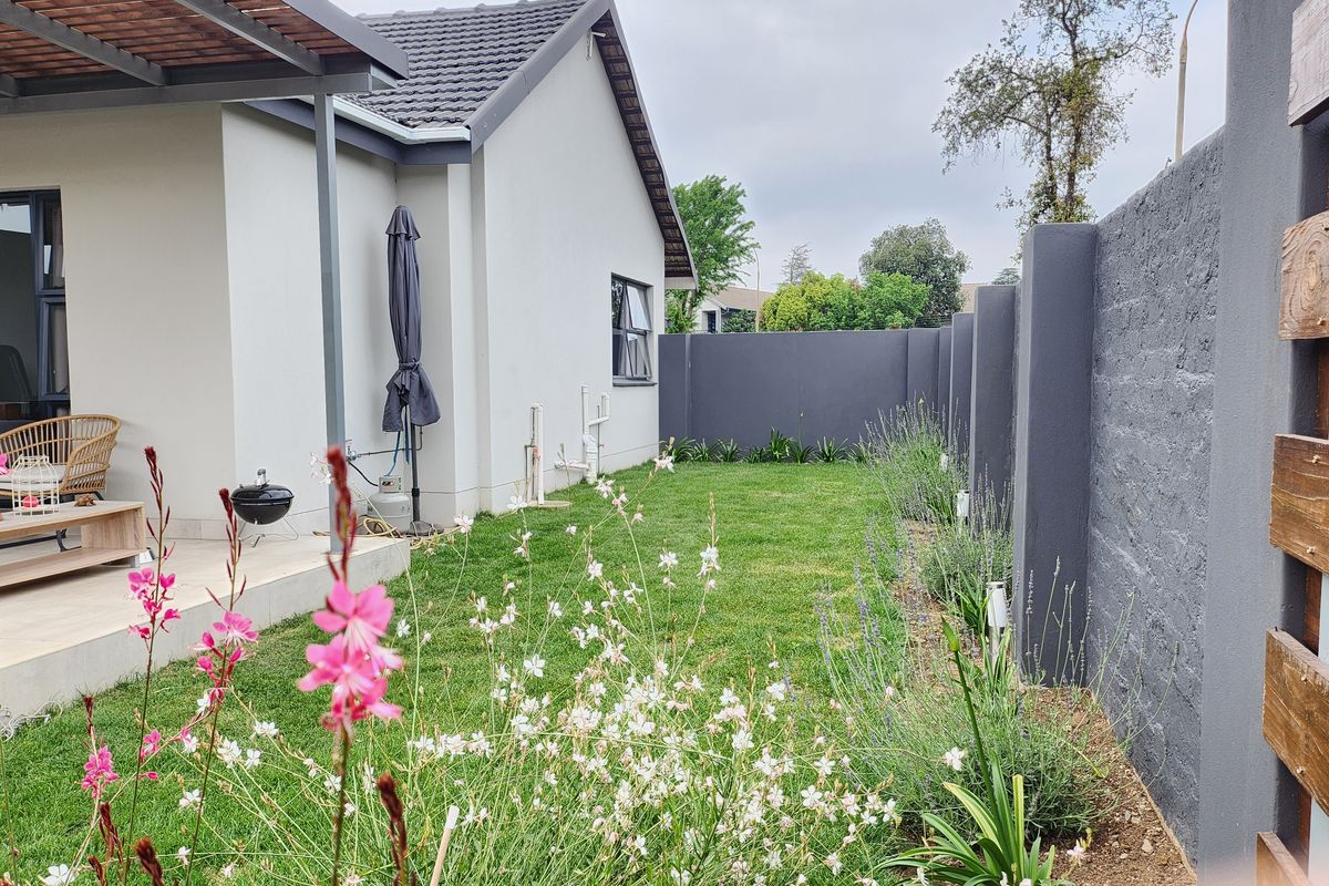 A well-maintained rear garden featuring a paved patio area, a manicured lawn, and a modern perimeter wall.