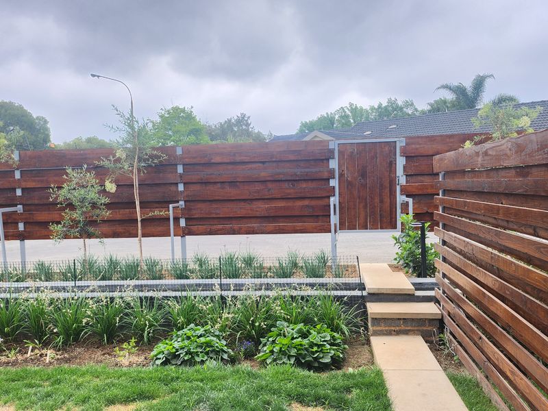 A well-maintained rear garden area featuring horizontal timber slat fencing, a secure pedestrian gate, and landscaped garden beds with concrete pathway steps.