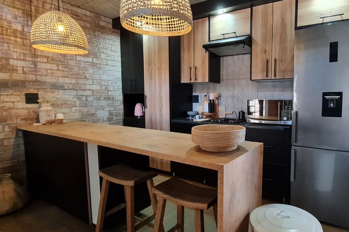 Modern kitchen featuring sleek two-tone cabinetry, a wooden breakfast bar, and an exposed brick feature wall, creating a contemporary and warm aesthetic.
