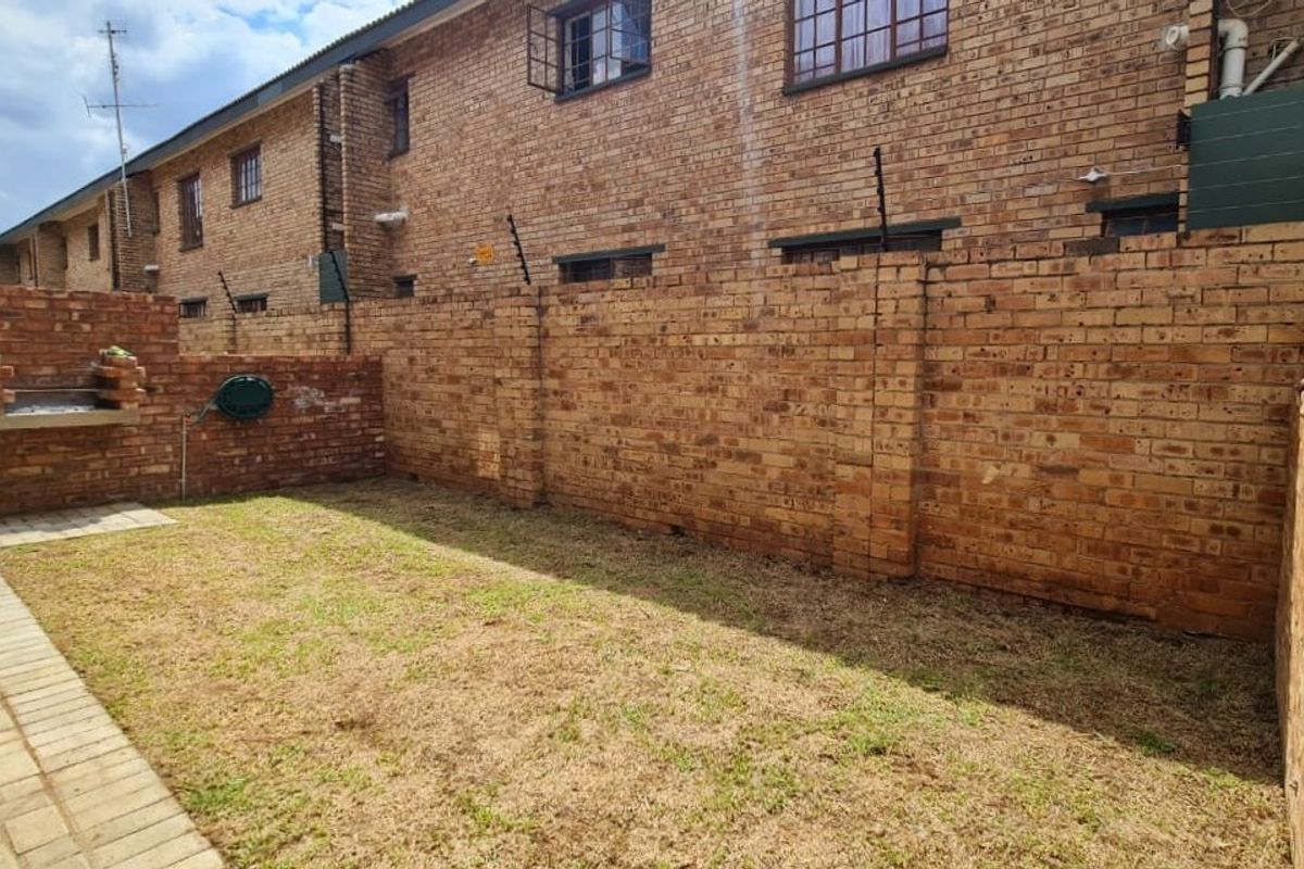 A private rear garden featuring a paved patio area, a built-in brick braai, and high brick boundary walls with electric fencing.