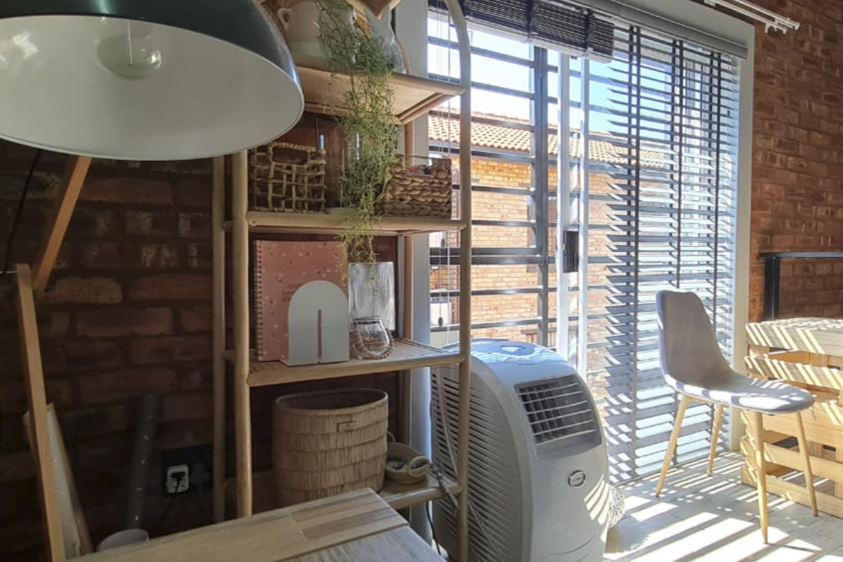 A living area featuring an exposed brick wall and a large sliding glass door with venetian blinds, providing natural light and access to the exterior.