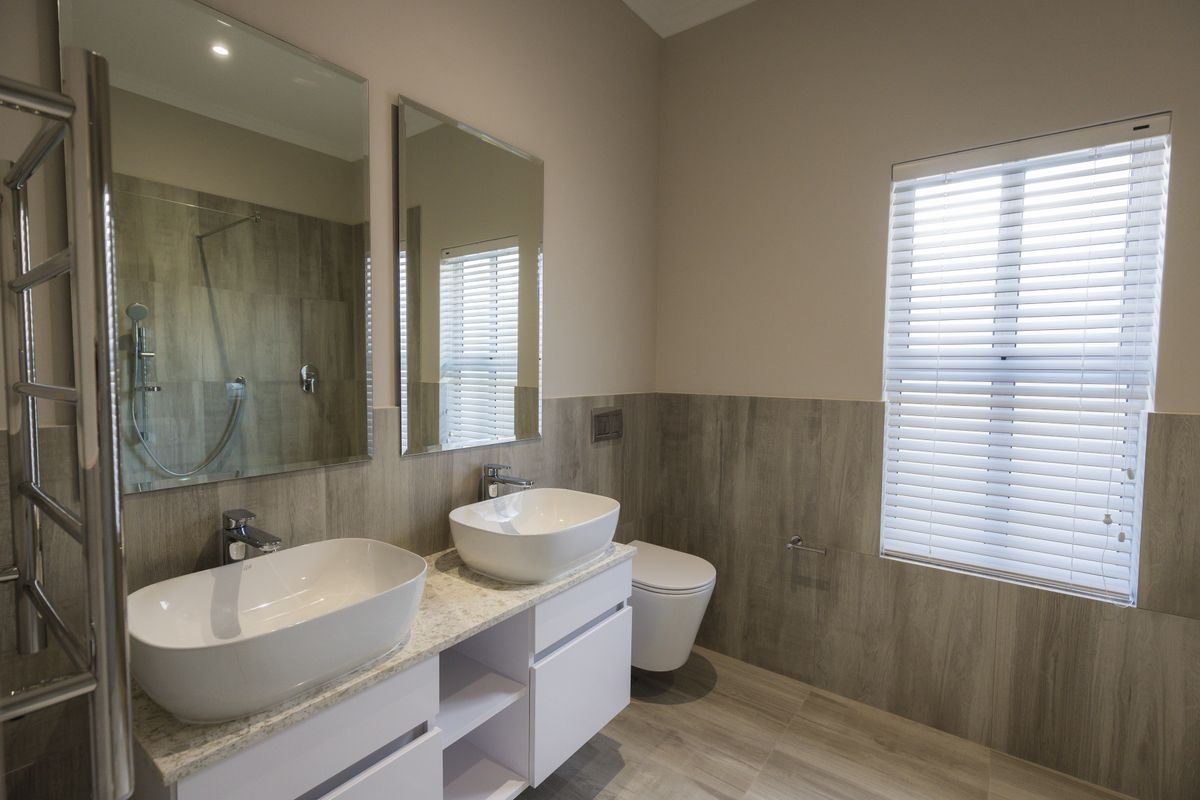Modern bathroom featuring a double vanity with vessel sinks, wall-hung toilet, walk-in shower, and a heated towel rail with neutral wood-look tiling.