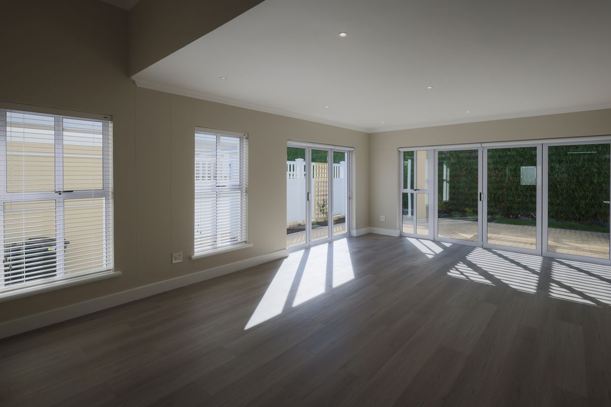 A bright and spacious open-plan living area featuring modern laminate flooring, recessed lighting, and large sliding glass doors providing access to the outdoor patio.