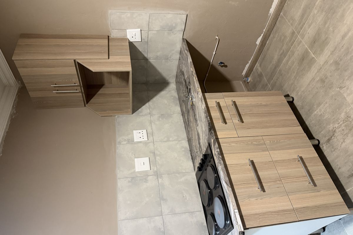 A compact kitchen area featuring wood-look cabinetry, a marble-effect countertop, an integrated electric hob, and neutral tiled backsplash.