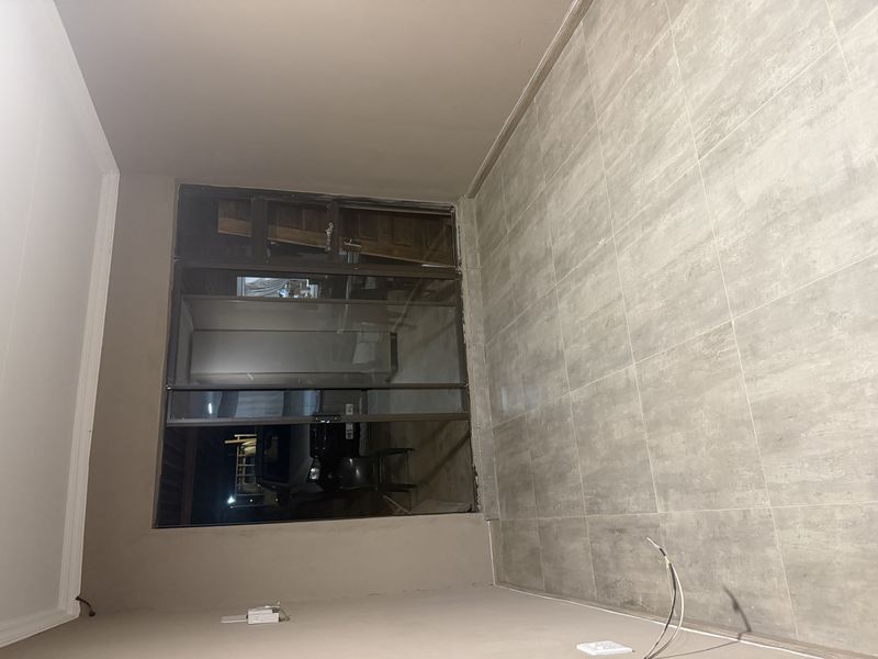An empty living room featuring neutral ceramic floor tiles and a large sliding glass door providing access to the exterior.