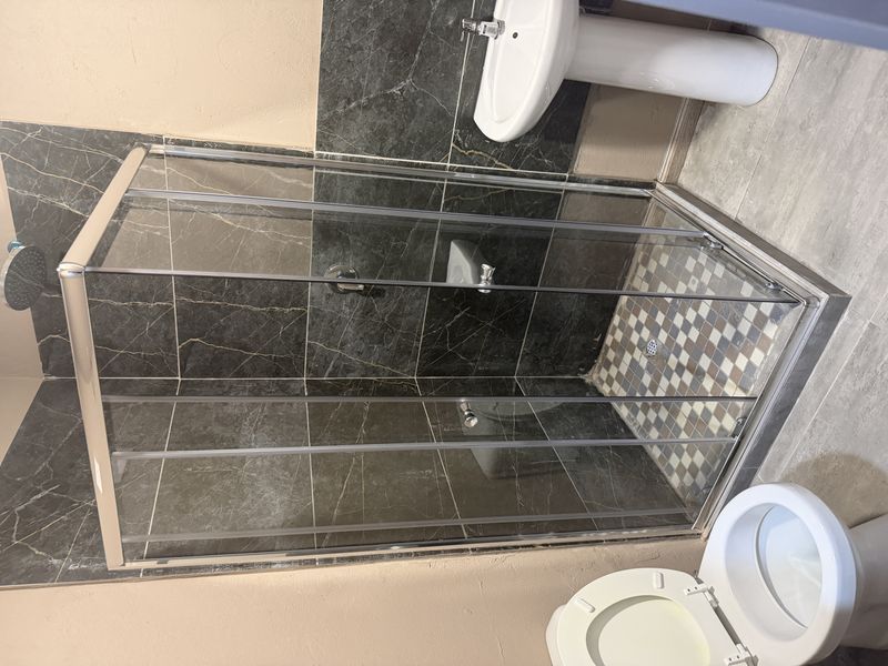 A compact bathroom featuring a corner shower enclosure with dark marble-effect wall tiles, a pedestal basin, and a standard toilet.