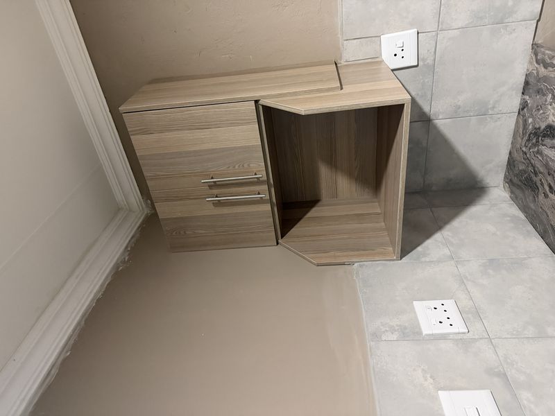 A kitchen corner featuring wall-mounted wood-look cabinetry, a tiled backsplash, and electrical outlets, showing minor unfinished paintwork near the ceiling.