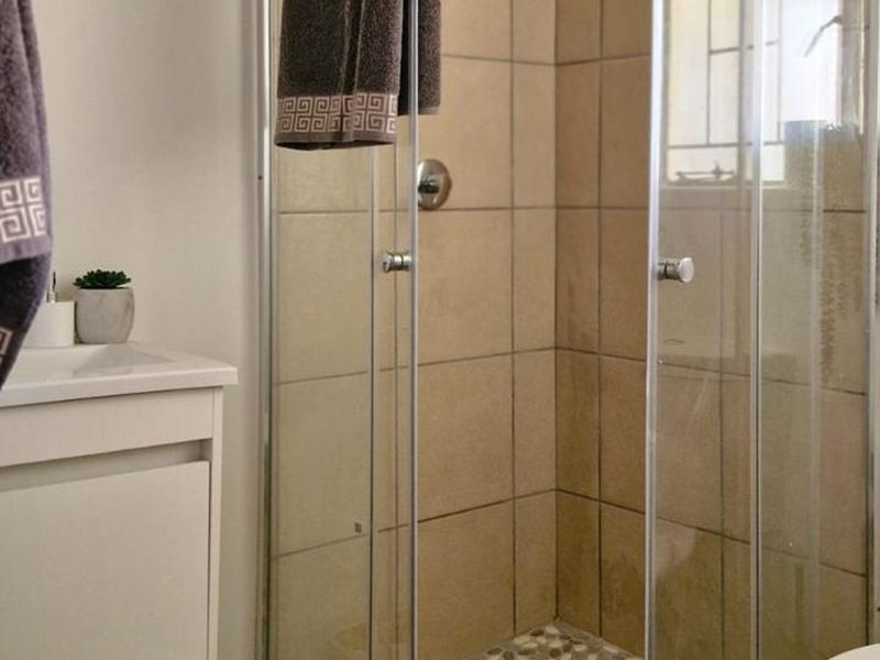 A functional bathroom featuring a glass-enclosed shower with neutral wall tiles, a pebble-style shower floor, and a white vanity cabinet.