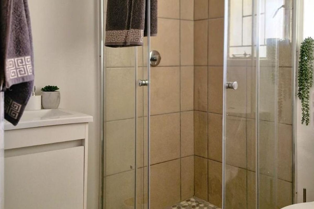 A functional bathroom featuring a glass-enclosed shower with neutral wall tiles, a pebble-style shower floor, and a white vanity cabinet.