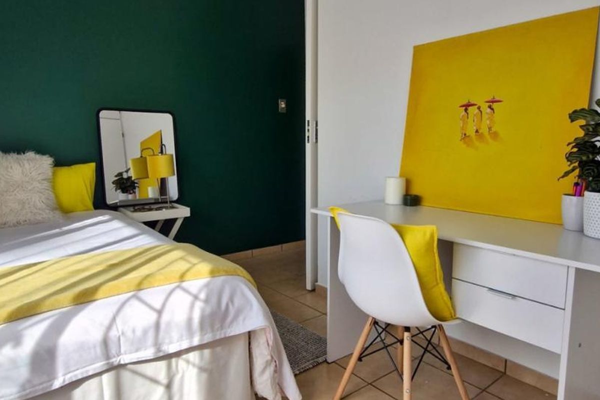 A bright bedroom featuring tiled flooring and a bold green accent wall, providing a clean and modern living space.
