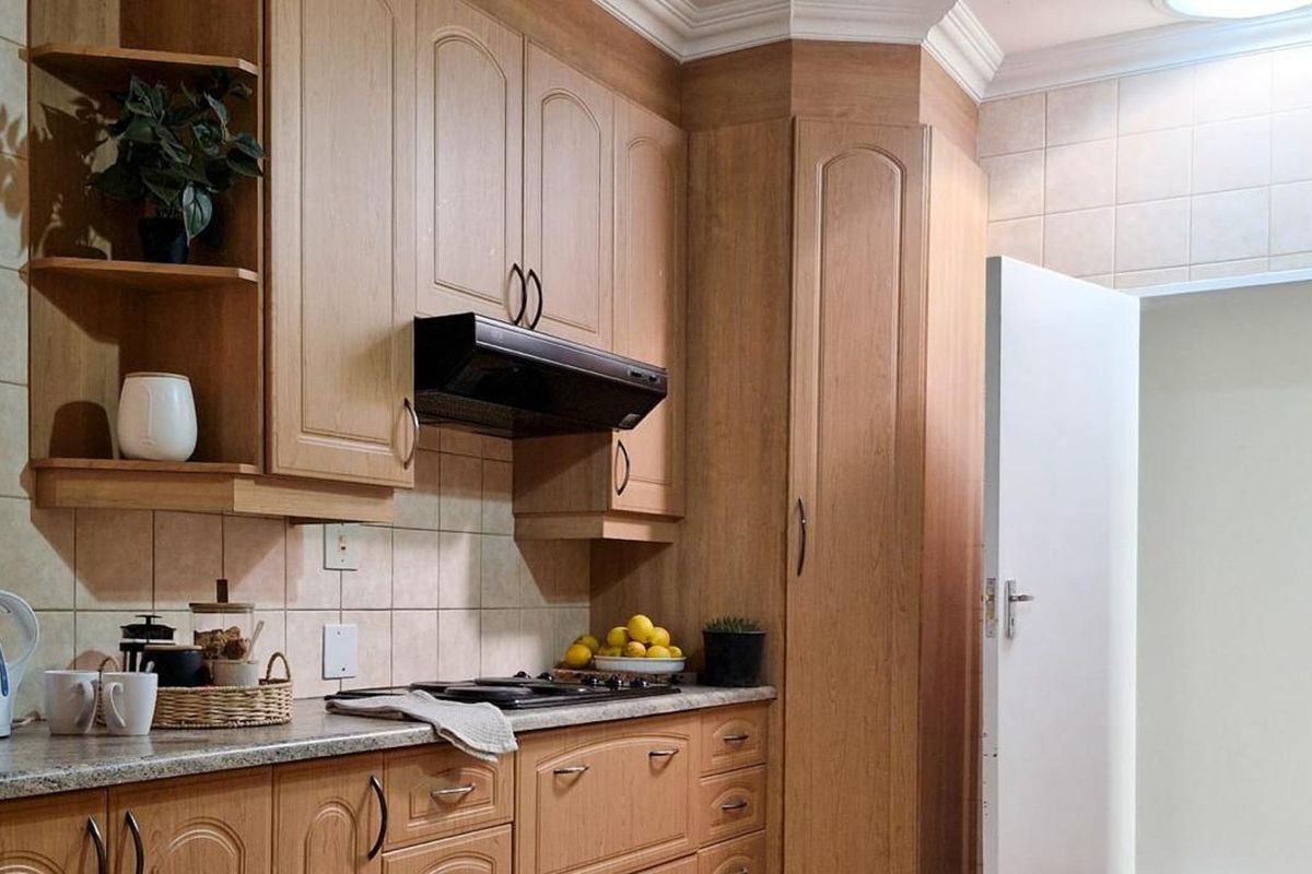 A functional kitchen featuring wood-finish cabinetry, tiled backsplash, and integrated hob with extractor fan.