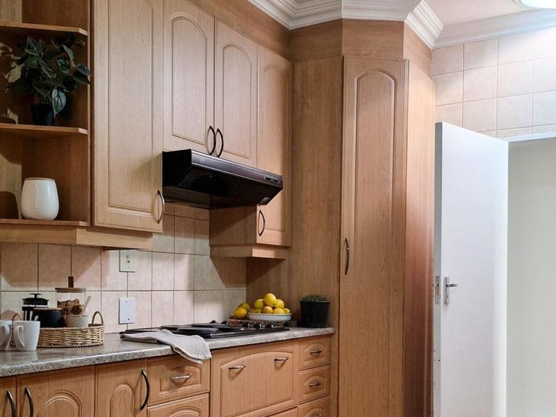 A functional kitchen featuring wood-finish cabinetry, tiled backsplash, and integrated hob with extractor fan.