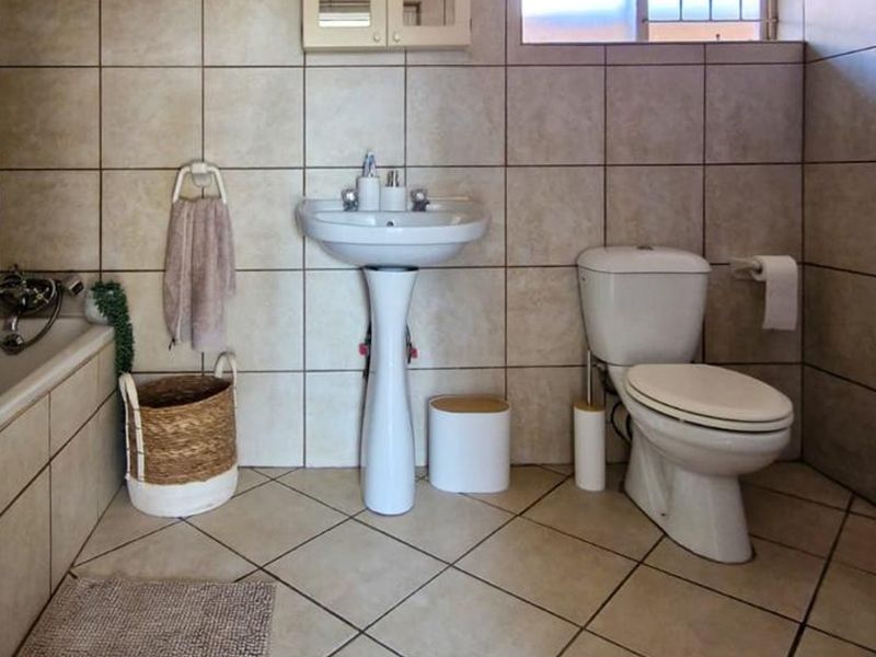 A functional bathroom featuring a pedestal basin, toilet, and bathtub with neutral ceramic wall and floor tiling.