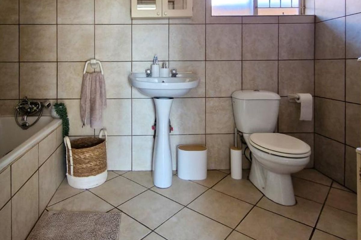 A functional bathroom featuring a pedestal basin, toilet, and bathtub with neutral ceramic wall and floor tiling.