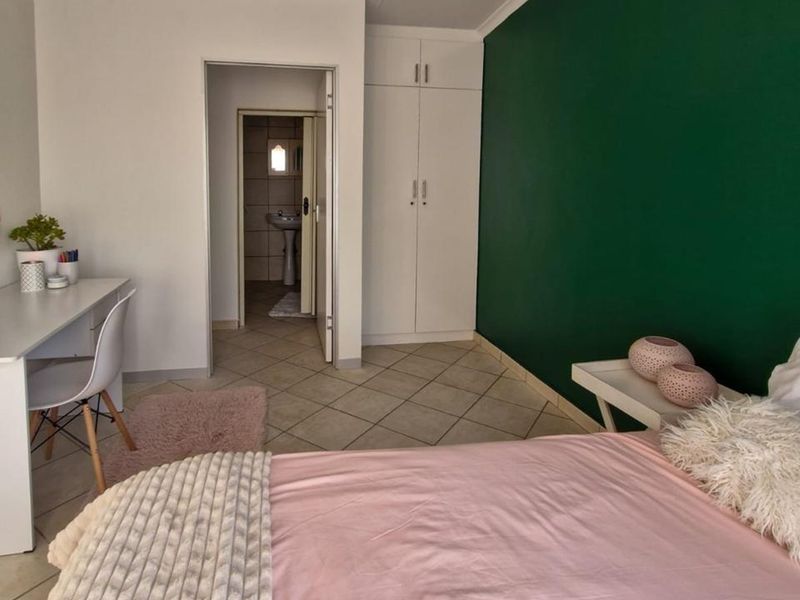 A bedroom featuring tiled flooring, a built-in wardrobe, and a green accent wall, with an adjoining bathroom visible through the doorway.