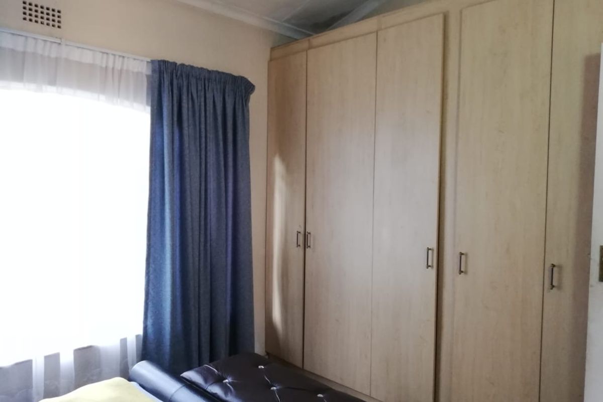 A bedroom featuring light wood-finish built-in cupboards and a window with curtains, showing signs of ceiling water damage.