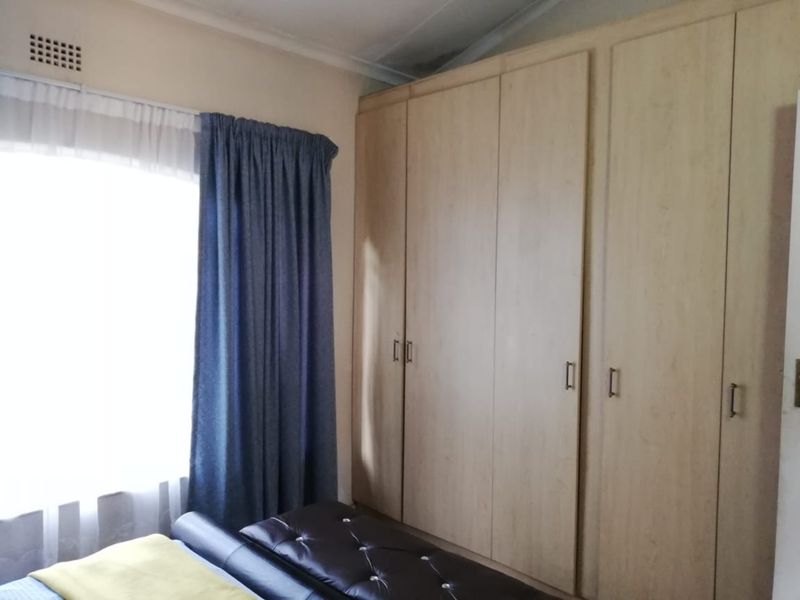 A bedroom featuring light wood-finish built-in cupboards and a window with curtains, showing signs of ceiling water damage.