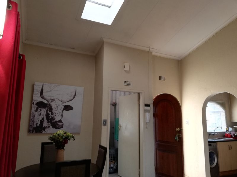 Open plan living area featuring a skylight, arched architectural details, and a solid wood entrance door, showing signs of wear on the ceiling finishes.