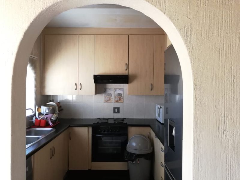 A compact kitchen featuring light wood-finish cabinetry, dark countertops, built-in oven and hob, and a distinctive arched entryway.