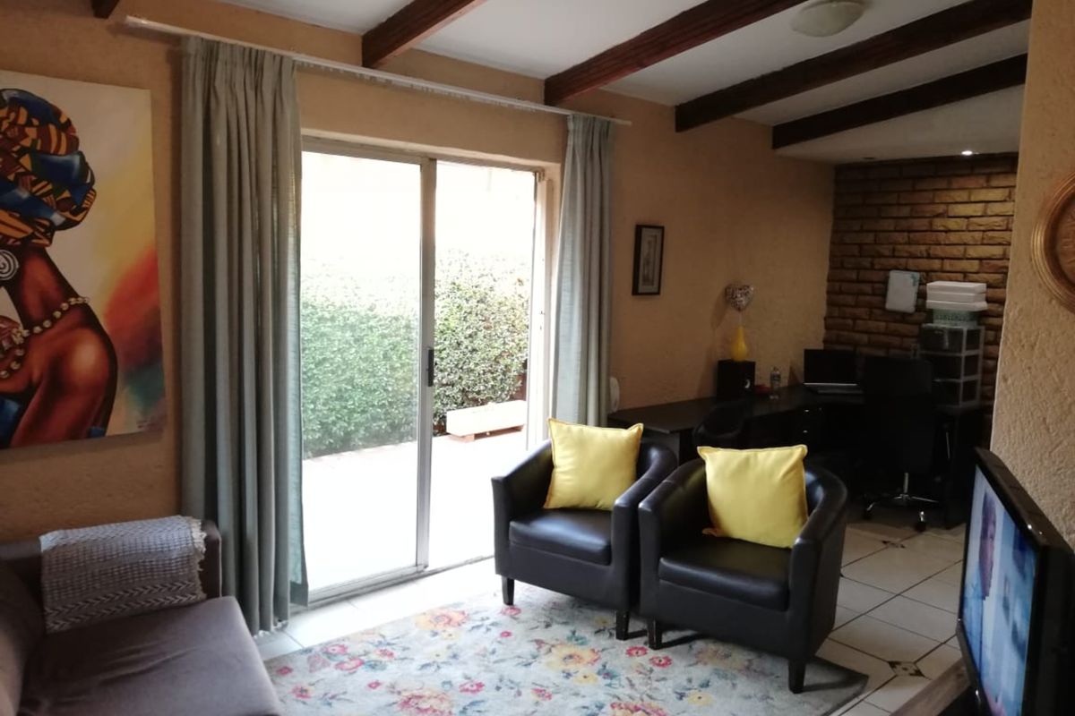 A living room featuring exposed timber ceiling beams, tiled flooring, and an exposed brick wall, with a sliding glass door leading to the exterior.