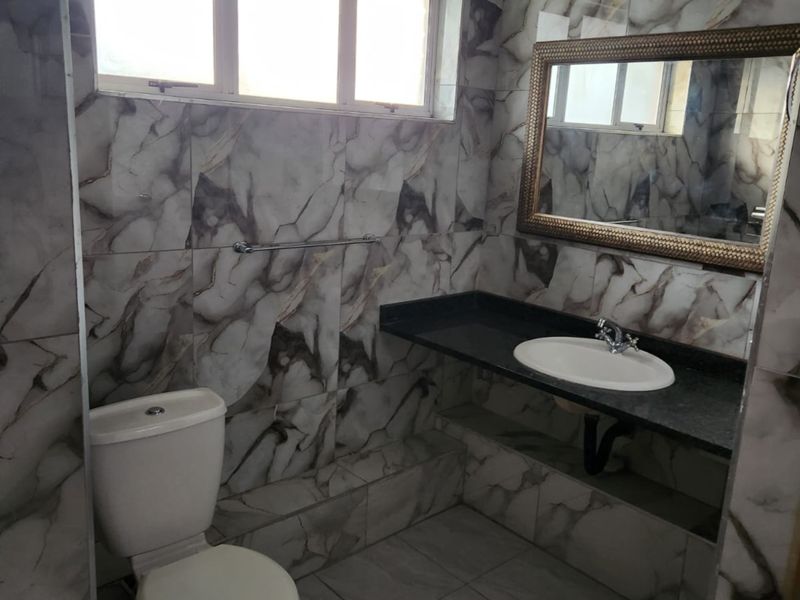 A bathroom featuring marble-effect wall tiling, a built-in vanity with a granite countertop, a ceramic basin, and a standard toilet.