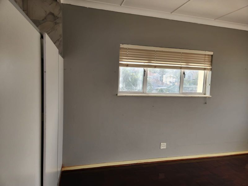 A bedroom featuring dark parquet flooring, built-in cupboards, and a window with fitted blinds.