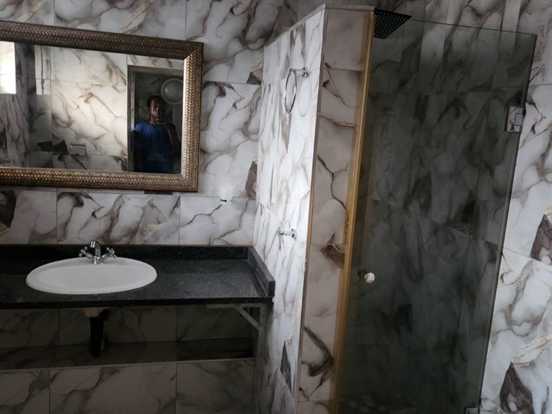 A bathroom featuring marble-effect wall tiles, a granite vanity top with a basin, and a glass-enclosed shower cubicle.